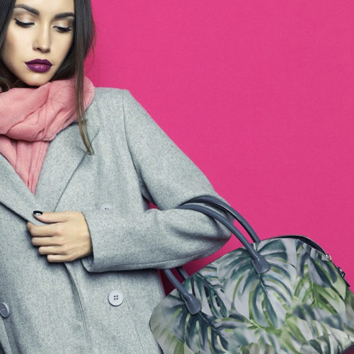 Fashion studio photo of young stylish woman on fuchsia background. Gray coat, pink scarf, purple lipstick, leather bag, . Catalogue clothes and accessories. Lookbook